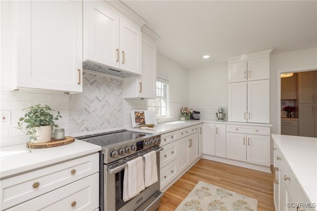Kitchen featuring light countertops, stainless steel range with electric stovetop, under cabinet range hood, light wood-style floors, and white cabinets | Image 13
