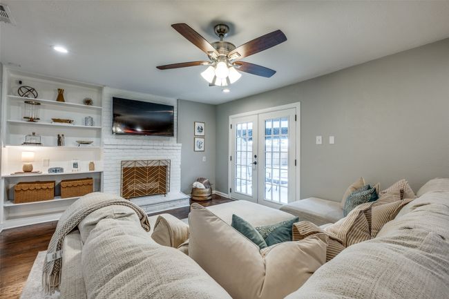 Living room with dark wood-style floors, a ceiling fan, french doors, a brick fireplace, and recessed lighting | Image 16
