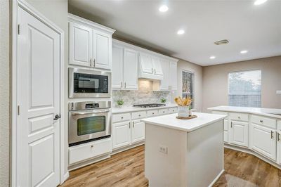 This updated kitchen features stunning quartz countertops that create an elegant and modern look. The marble backsplash adds a luxurious touch, tying together the crisp white cabinetry and gold hardware. | Image 2