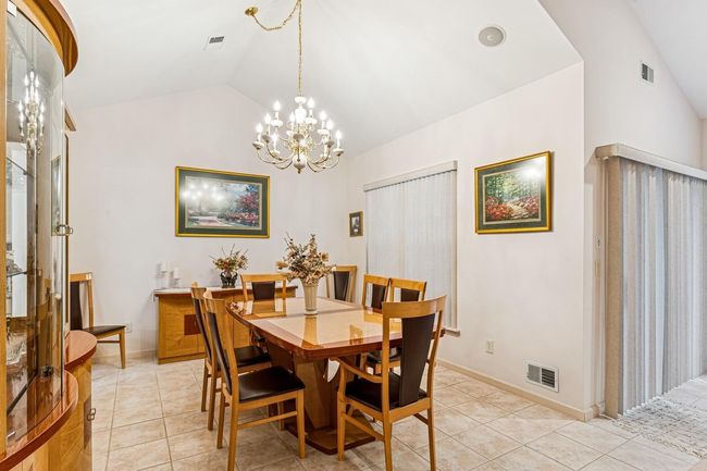 Dining area with light tile patterned flooring, visible vents, vaulted ceiling, and a notable chandelier | Image 11