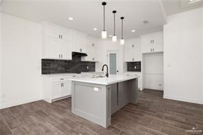 Kitchen with a kitchen island with sink, tasteful backsplash, recessed lighting, white cabinetry, and light countertops | Image 7