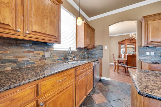 Kitchen with stainless steel dishwasher, arched walkways, ornamental molding, brown cabinets, and backsplash | Image 13