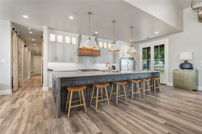 Kitchen featuring premium range hood, appliances with stainless steel finishes, a barn door, white cabinets, and light wood-style floors | Image 9