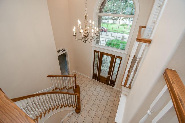 Spacious two-story foyer with elegant curved staircase, large decorative window, and chandelier. The entrance features double doors with glass panels, and the area is tiled for a grand impression. | Image 10