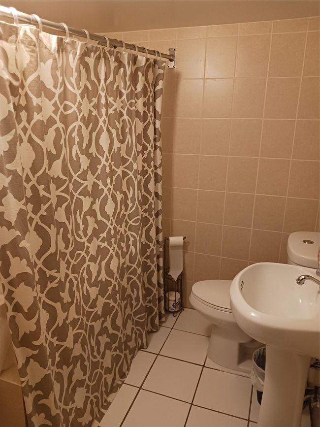 Bathroom with tile walls, curtained shower, toilet, and tile patterned flooring | Image 23