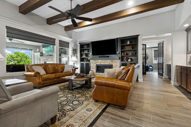 Living room with ceiling fan, beamed ceiling, a stone fireplace, light wood-style flooring, and recessed lighting | Image 9