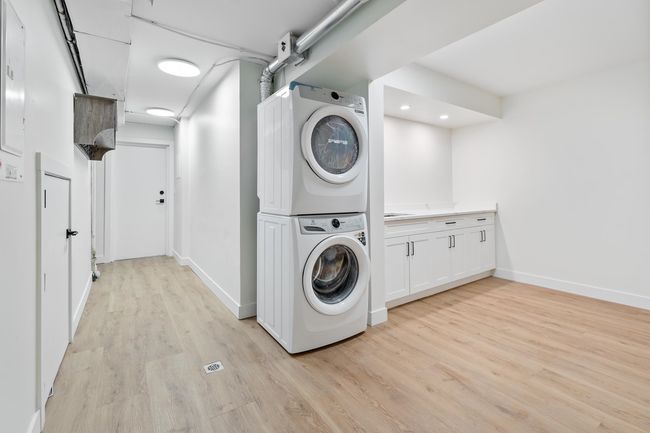 Laundry area featuring stacked washer and clothes dryer, recessed lighting, cabinet space, light wood finished floors, and baseboards | Image 19