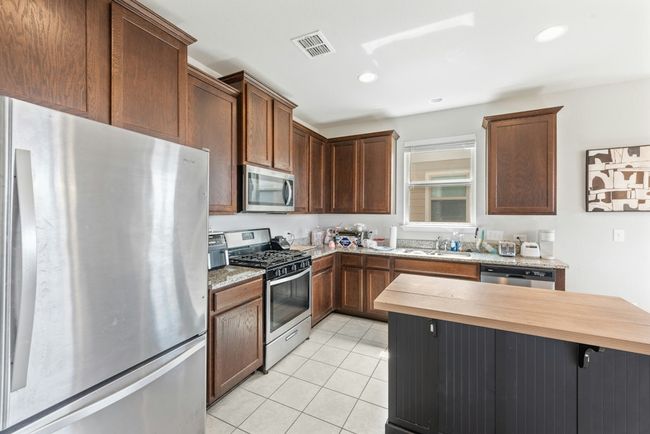 Kitchen featuring light tile patterned floors, visible vents, butcher block countertops, a sink, and appliances with stainless steel finishes | Image 7