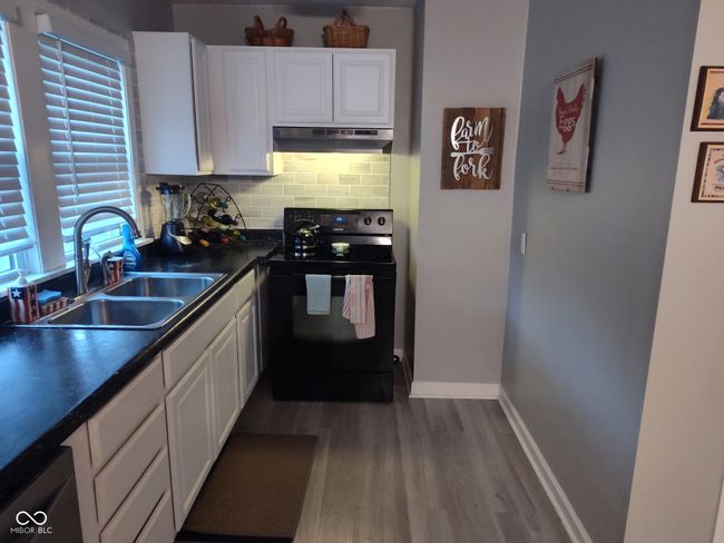 kitchen featuring black electric range, under cabinet range hood, a sink, dark countertops, and white cabinets | Image 6