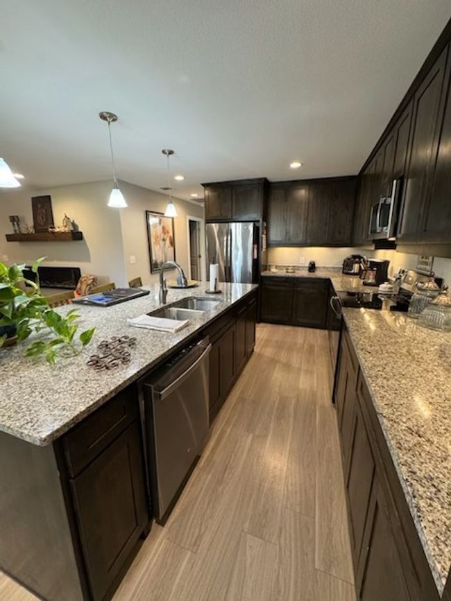 Kitchen featuring light wood-style floors, appliances with stainless steel finishes, a sink, and light stone countertops | Image 11