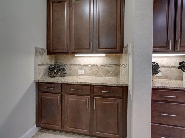 Kitchen with tasteful backsplash, light stone counters, and dark brown cabinets | Image 9