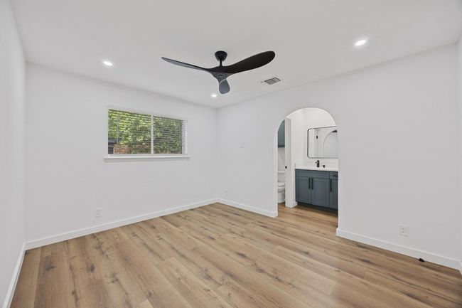 Primary bedroom with arched walkways, ceiling fan, light wood-style floors, and recessed lighting | Image 17