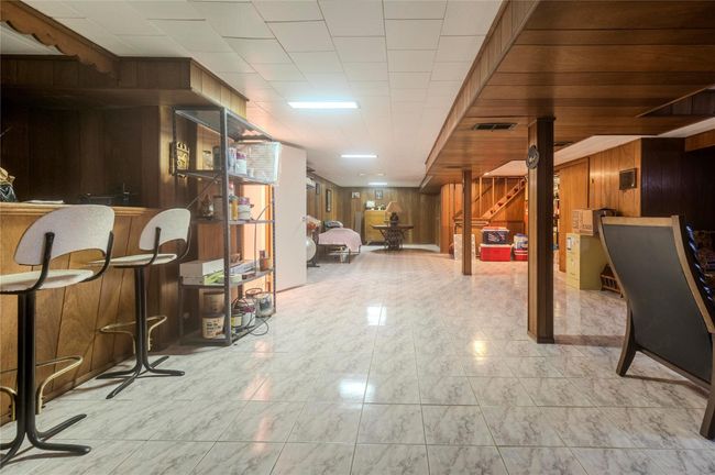 Finished basement with visible vents, stairs, bar, wood walls, and marble finish floor | Image 26