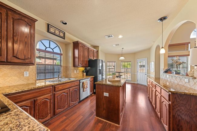 Kitchen featuring a center island, a sink, appliances with stainless steel finishes, light stone countertops, and dark wood-type flooring | Image 10