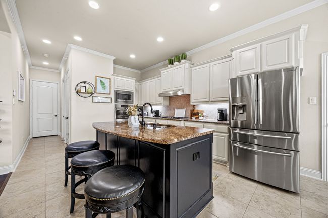 Kitchen featuring stainless steel appliances, granite countertops, baseboards, backsplash, and white cabinetry | Image 7