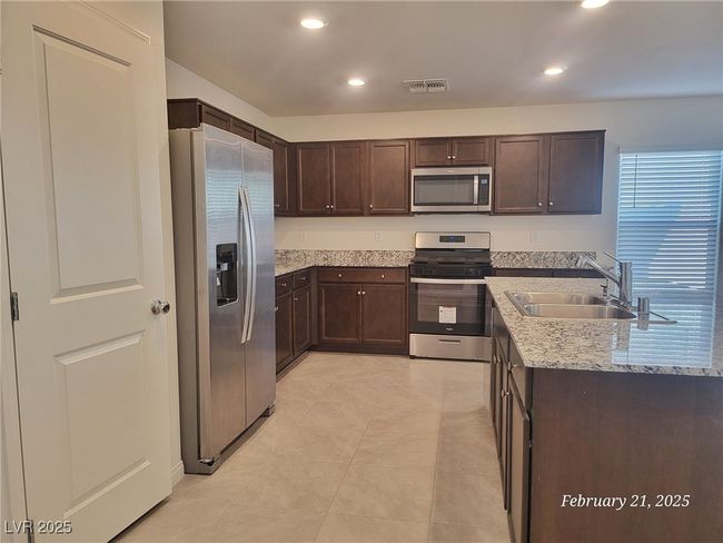 Kitchen featuring light stone counters, visible vents, appliances with stainless steel finishes, dark brown cabinetry, and a sink | Image 4