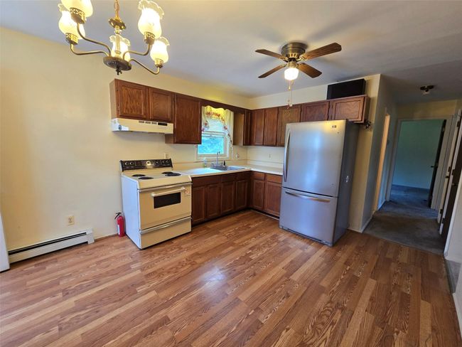 Kitchen with freestanding refrigerator, electric stove, under cabinet range hood, a sink, and baseboard heating | Image 12
