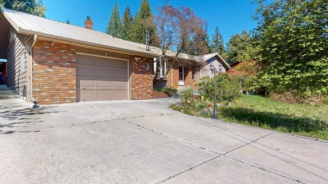 Single story home featuring a chimney, metal roof, concrete driveway, a garage, and brick siding | Image 29