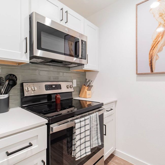 Kitchen featuring decorative backsplash, light countertops, white cabinets, and stainless steel appliances | Image 4
