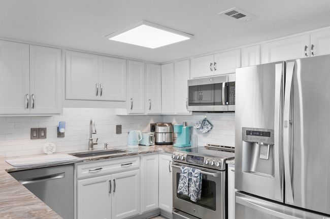 Kitchen with stainless steel appliances, a sink, white cabinets, backsplash, and light stone counters | Image 4
