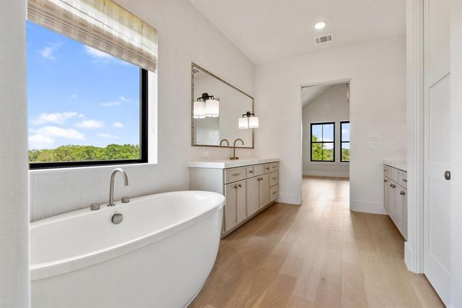 Experience luxury in the primary bathroom featuring a soaking tub, dual vanities, and an oversized frameless glass shower. Enjoy serene pasture views through the window. To the left is a water closet and very large closet. | Image 21