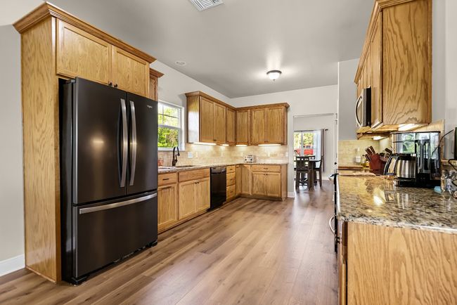 Kitchen with freestanding refrigerator, light wood-type flooring, light stone counters, stainless steel microwave, and decorative backsplash | Image 10