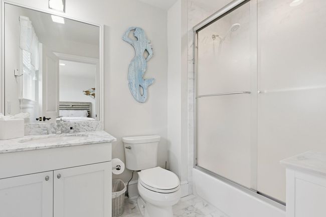 Bathroom featuring marble look tiles, vanity, toilet, shower / bath combination with glass door, and ensuite bathroom | Image 17
