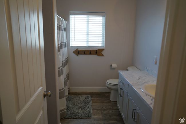 Bathroom with a shower with curtain, vanity, toilet, baseboards, and wood finished floors | Image 12