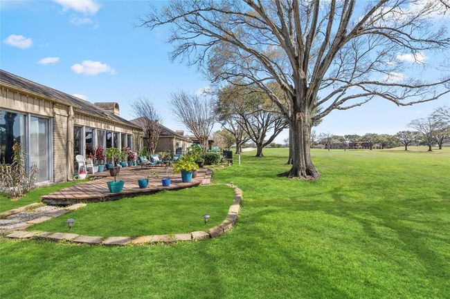 Expansive backyard retreat with a spacious wooden deck, seamlessly blending into the lush greenery of the golf course. Mature trees provide natural shade, while the landscaped stone pathway and garden beds add character to the outdoor space. A perfect setting for relaxation and enjoying scenic views. | Image 38