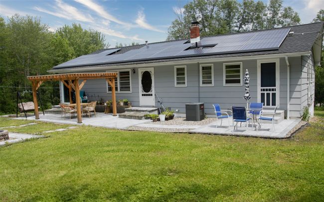 Rear view of house with a patio area, a lawn, a chimney, roof mounted solar panels, and central AC | Image 4