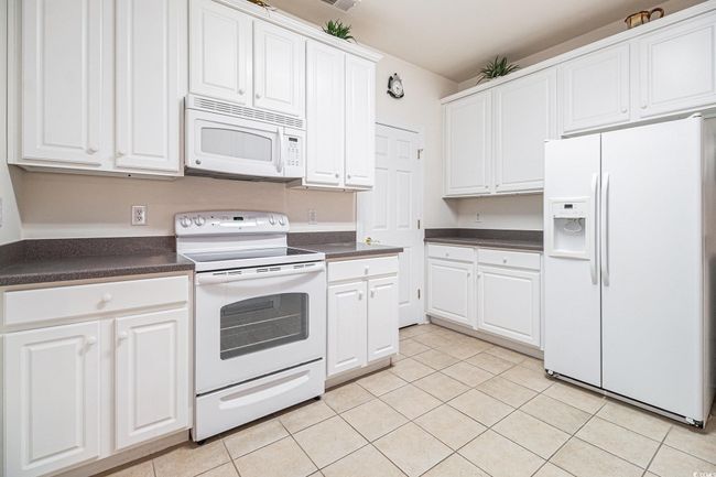 Kitchen featuring white appliances, dark countertops, light tile patterned floors, and white cabinets | Image 9