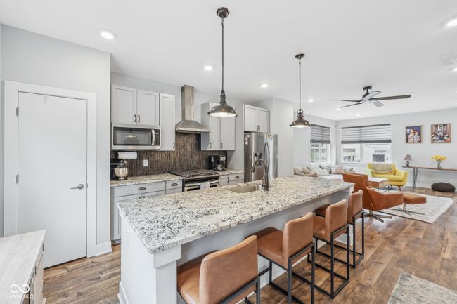 kitchen featuring stainless steel appliances, a ceiling fan, a sink, wall chimney range hood, and a kitchen breakfast bar | Image 6