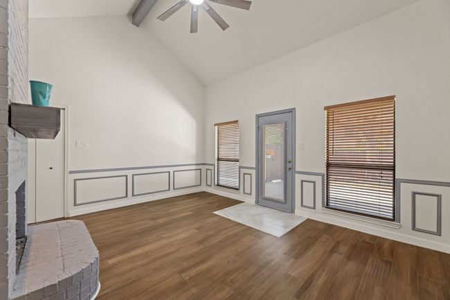 Unfurnished living room featuring a wainscoted wall, beamed ceiling, a fireplace, wood finished floors, and a ceiling fan | Image 17