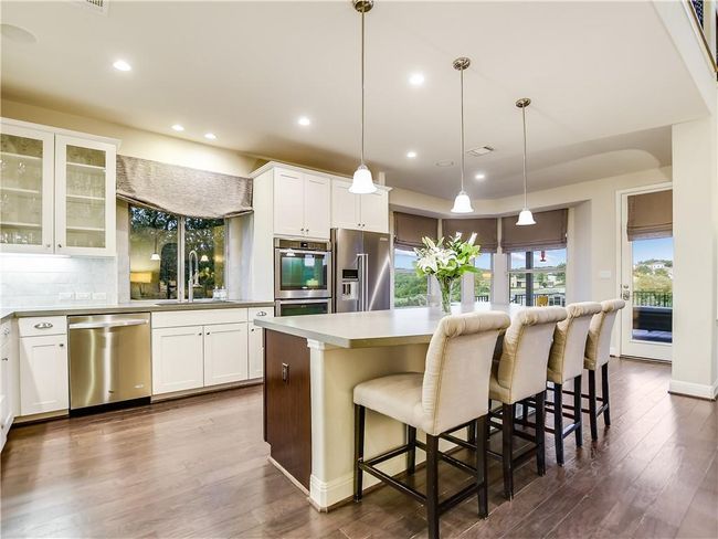 Kitchen featuring appliances with stainless steel finishes, backsplash, a kitchen island, white cabinetry, and dark wood-style floors | Image 20