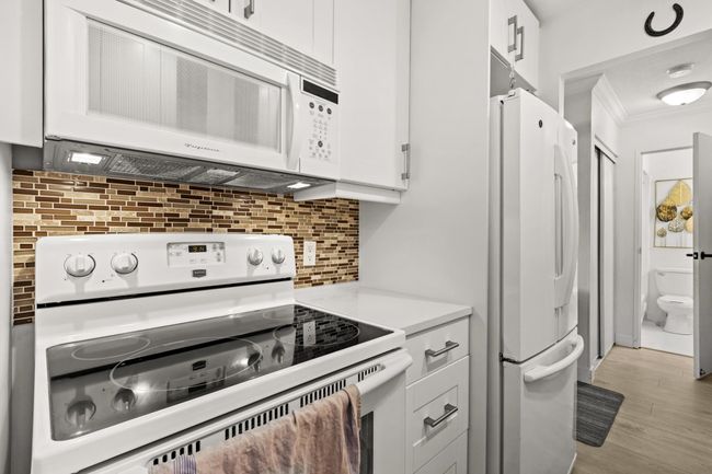 Kitchen featuring light countertops, ornamental molding, decorative backsplash, white cabinets, and white appliances | Image 12