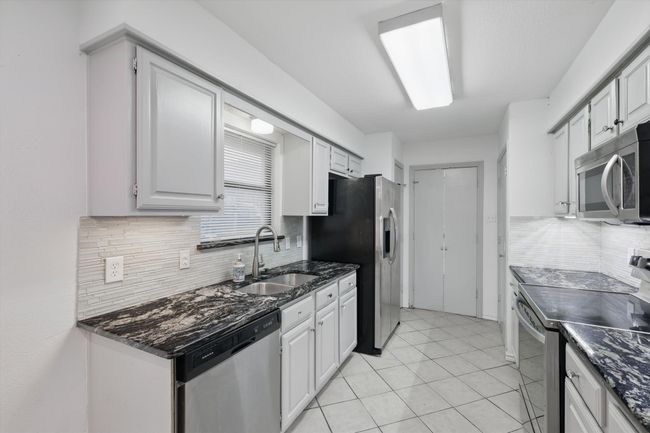 Kitchen featuring appliances with stainless steel finishes, decorative backsplash, light tile patterned floors, and dark stone countertops | Image 7