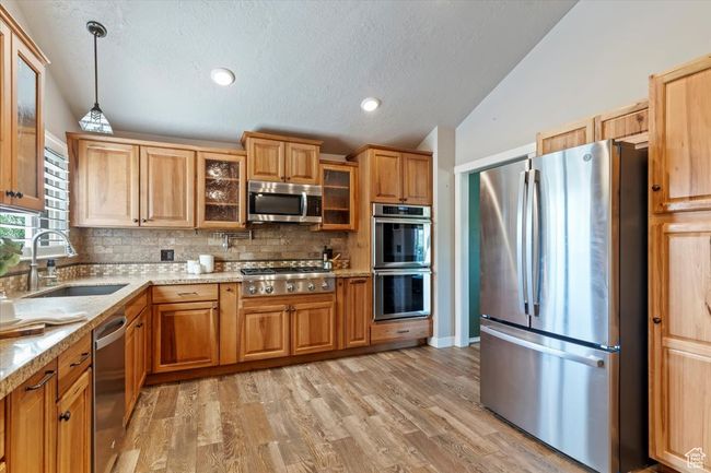 Kitchen with appliances with stainless steel finishes, a sink, vaulted ceiling, backsplash, and decorative light fixtures | Image 12