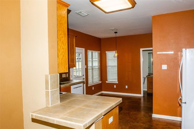 Kitchen with white appliances, brown cabinetry, finished concrete flooring, hanging light fixtures, and a peninsula | Image 5