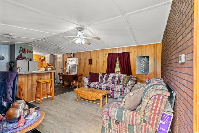 Living room with wood walls, wood finished floors, vaulted ceiling, and ceiling fan | Image 5