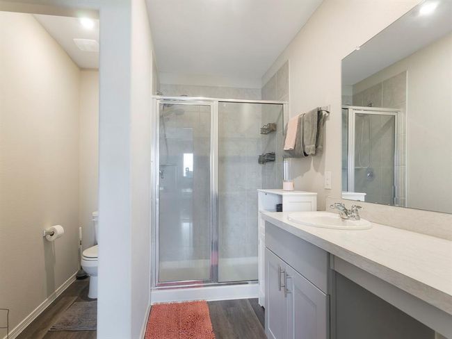 This en suite bathroom features a modern design with a spacious glass-enclosed shower, a single vanity with ample counter space, and neutral tones for a clean, bright look. The area includes a separate toilet space for added privacy. | Image 14