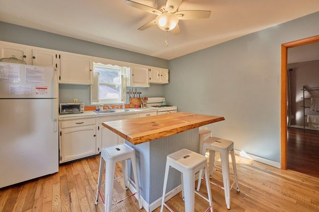 Kitchen featuring white appliances, white cabinetry, a kitchen breakfast bar, and a sink | Image 4