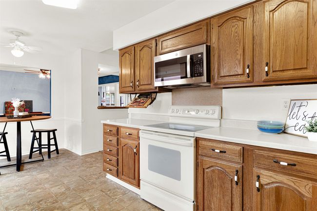 Kitchen featuring white electric range, stainless steel microwave, brown cabinets, ceiling fan, and light countertops | Image 31