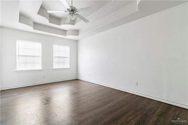 Empty room featuring a raised ceiling, dark wood finished floors, and ceiling fan | Image 15