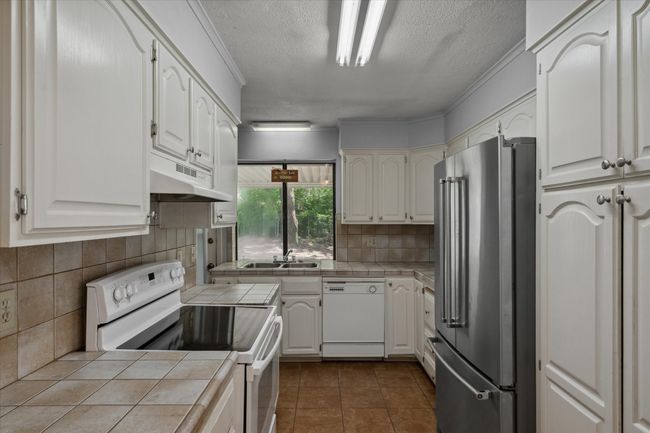 Kitchen featuring white appliances, tile counters, under cabinet range hood, a textured ceiling, and tasteful backsplash | Image 21