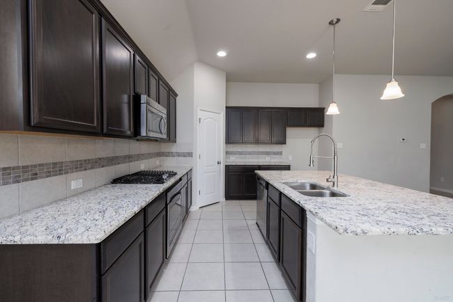 Kitchen featuring appliances with stainless steel finishes, tasteful backsplash, arched walkways, light tile patterned floors, and hanging light fixtures | Image 8