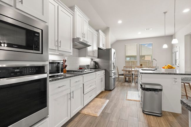 Kitchen featuring stainless steel appliances, white cabinetry, dark stone countertops, tasteful backsplash, and a kitchen island with sink | Image 7