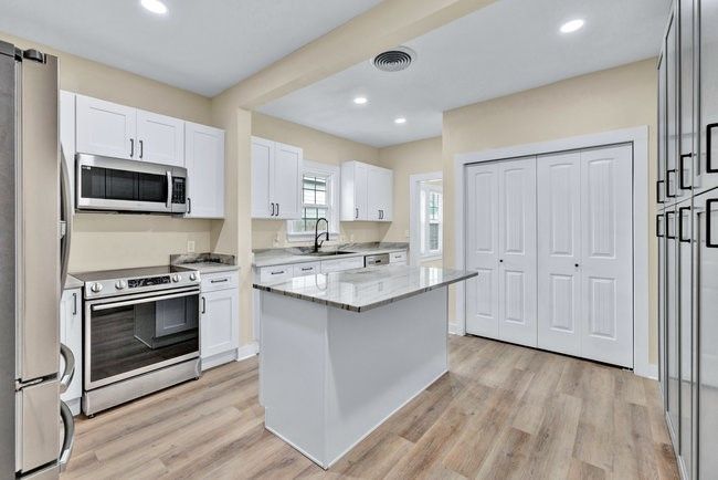 Kitchen featuring a sink, stainless steel appliances, light stone counters, white cabinetry, and a kitchen island | Image 11
