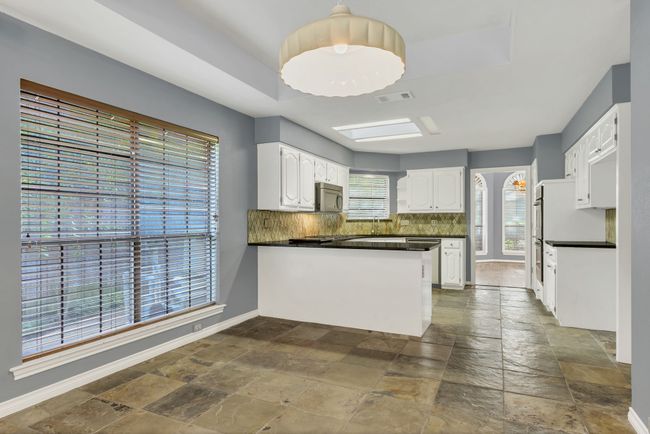 Kitchen featuring appliances with stainless steel finishes, stone tile flooring, a peninsula, and backsplash | Image 13