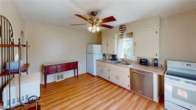 Kitchen featuring white appliances, light wood-type flooring, sink, and white cabinetry | Image 3