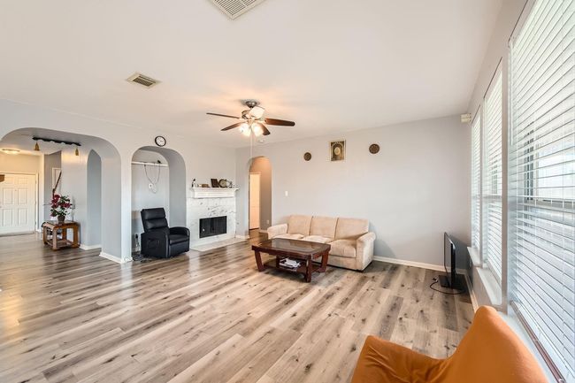 Spacious open concept living room with light wood flooring, a cozy fireplace, and tons of natural light from the large windows. | Image 8